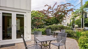 A patio with outdoor furniture, a white building with glass doors, and a tree with red leaves.