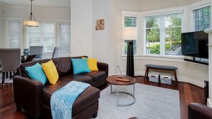 A living room with a brown leather sofa, a round coffee table, a television, and a dining area with a table and chairs.