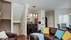 A living room with a brown leather sofa, a coffee table, and a staircase leading to a kitchen area.