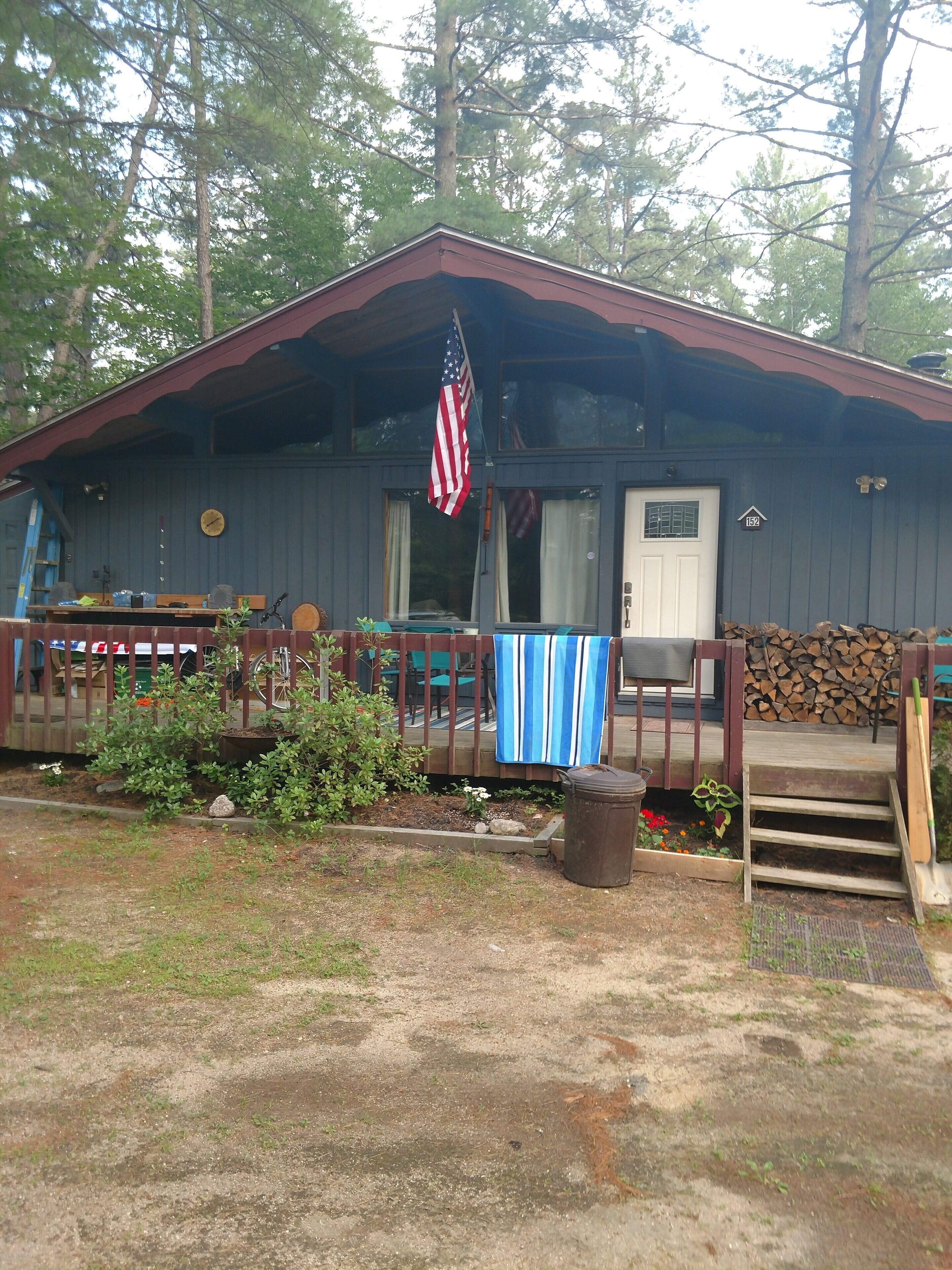 A cabin with a porch, a flag, and a number sign.