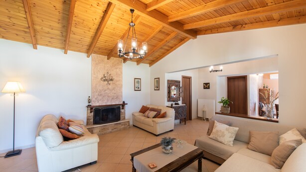 A spacious living room with a fireplace, wooden ceiling beams, and a cozy seating area. -  Villa Pine Forest  (Corfu)