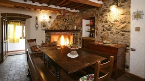 Un comedor rústico con pared de piedra, vigas de madera en el techo, chimenea y una mesa de madera con bancos.