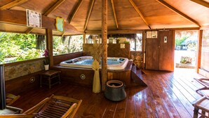 Zona de spa con techo de madera, dos jacuzzis, asientos de madera y una pared de piedra.