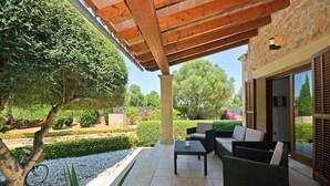 Eine überdachte Terrasse mit Gartenmöbeln, einer Steinmauer und einem Garten mit verschiedenen Pflanzen und einem Baum.