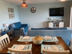 Una sala de estar acogedora con un sofá, una mesa de comedor servida con platos y vasos, un televisor y un reloj de pared decorativo.