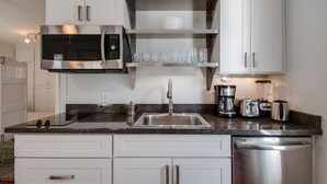 Una cocina moderna con armarios blancos, un microondas de acero inoxidable, un lavabo y un lavavajillas.
