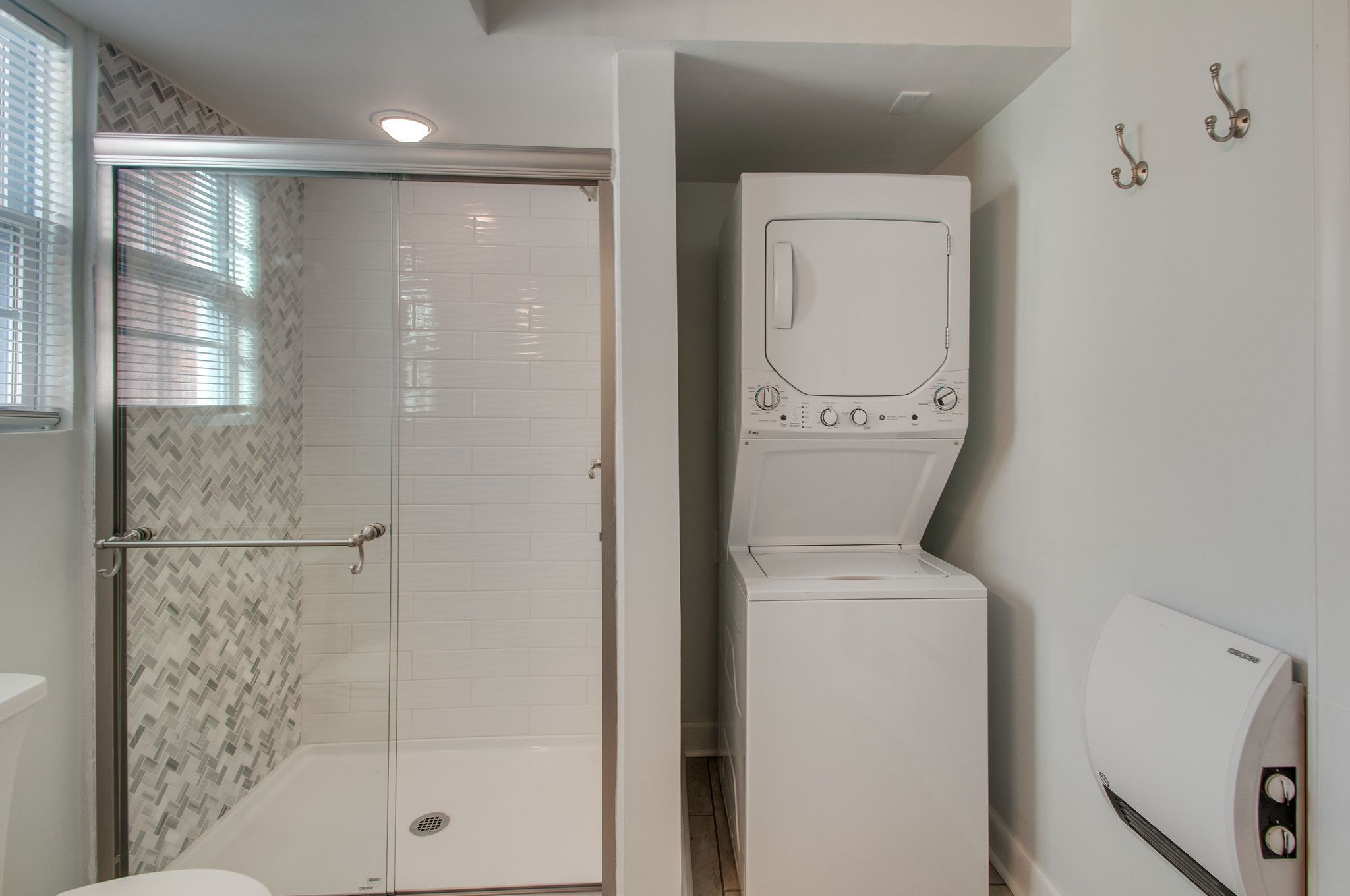 A bathroom with a shower, a washing machine, and a hand dryer.