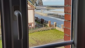 A coastal view through a window, featuring a road, a brick building, and a cliff. - "FACING THE SEA" VEULETTES SUR MER APARTMENT (Veulettes-sur-Mer)
