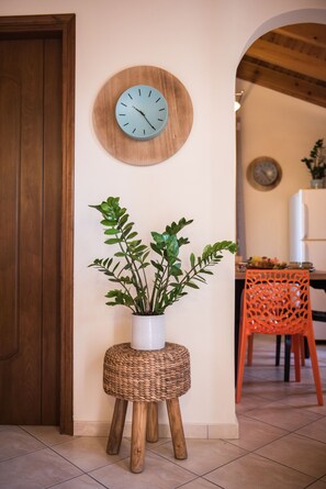 A room with a wooden door, a wall-mounted clock, a potted plant, and a dining area with a chair and table.