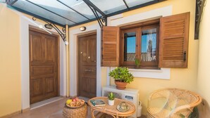Eine überdachte Terrasse mit Holztüren, einem Tisch mit einer Pflanze, Korbstühlen und einem Obstkorb.