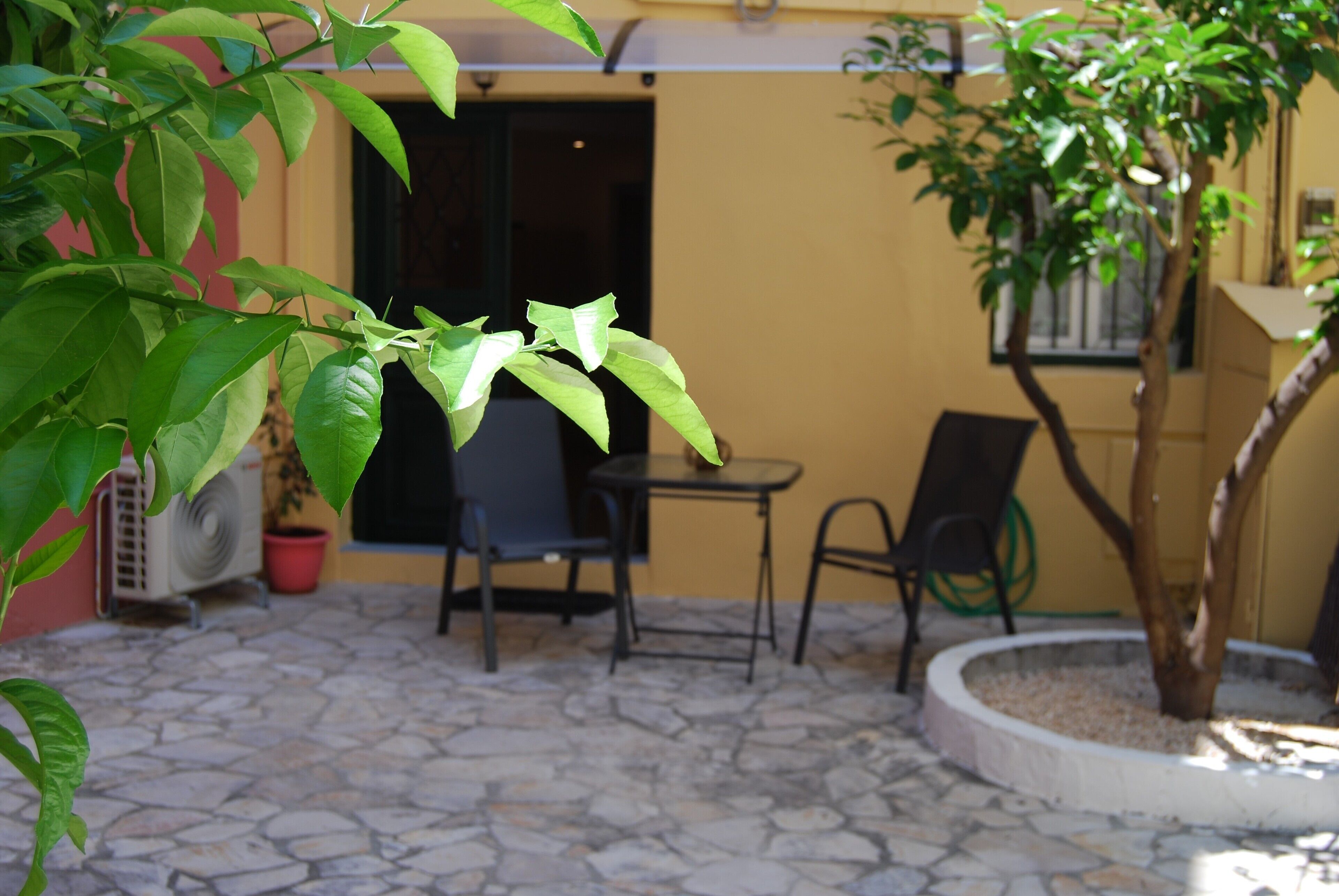 A patio area with stone flooring, two chairs, a small table, and a potted plant.