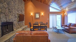 Ein gemütliches Wohnzimmer mit Kamin aus Stein, einer Essecke mit Tisch und Stühlen, einem Ledersofa und einem großen Fenster, das für natürliches Licht sorgt.