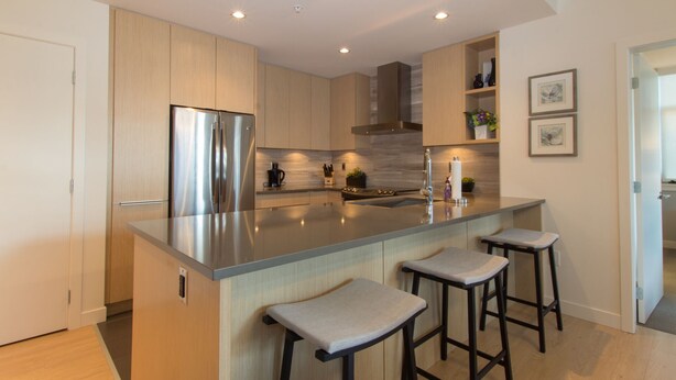 A modern kitchen with a large island, stainless steel appliances, and bar stools. - Duet Delight-Beautiful Double Ensuite Condo in James Bay, Wonderful Neighbourhood by Victoria Prime! (Victoria)