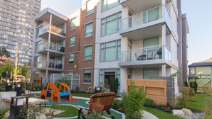 A modern apartment building with multiple balconies, a children's play area, and a well-maintained garden. - Duet Delight-Beautiful Double Ensuite Condo in James Bay, Wonderful Neighbourhood by Victoria Prime! (Victoria)