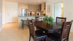 A modern kitchen with stainless steel appliances, wooden cabinets, and a dining area with a dark wooden table and chairs. - Duet Delight-Beautiful Double Ensuite Condo in James Bay, Wonderful Neighbourhood by Victoria Prime! (Victoria)