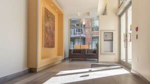 A modern lobby with a large abstract painting, a seating area with sofas, and a view of the outside building. - Duet Delight-Beautiful Double Ensuite Condo in James Bay, Wonderful Neighbourhood by Victoria Prime! (Victoria)