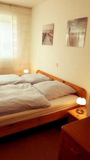 Une chambre d’hôtel avec un lit en bois, deux lampes de chevet et deux tableaux encadrés au mur.