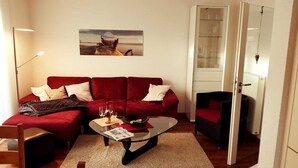 Ein Wohnzimmer mit einem roten Sofa, einem Glastisch und einem Gemälde an der Wand.
