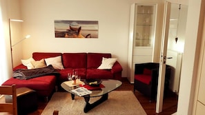 Un salon avec un canapé rouge, une table basse en verre et un tableau accroché au mur.