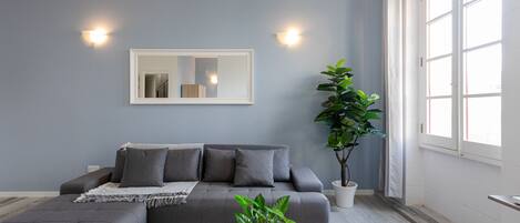 Una sala de estar moderna con un sofá gris, una mesa de centro blanca y una planta grande en maceta.