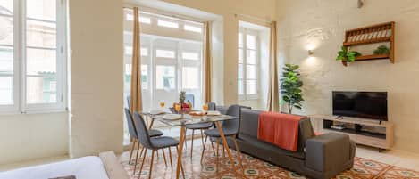 A room with a bed, a sofa, a TV, a dining table with chairs, and a window.