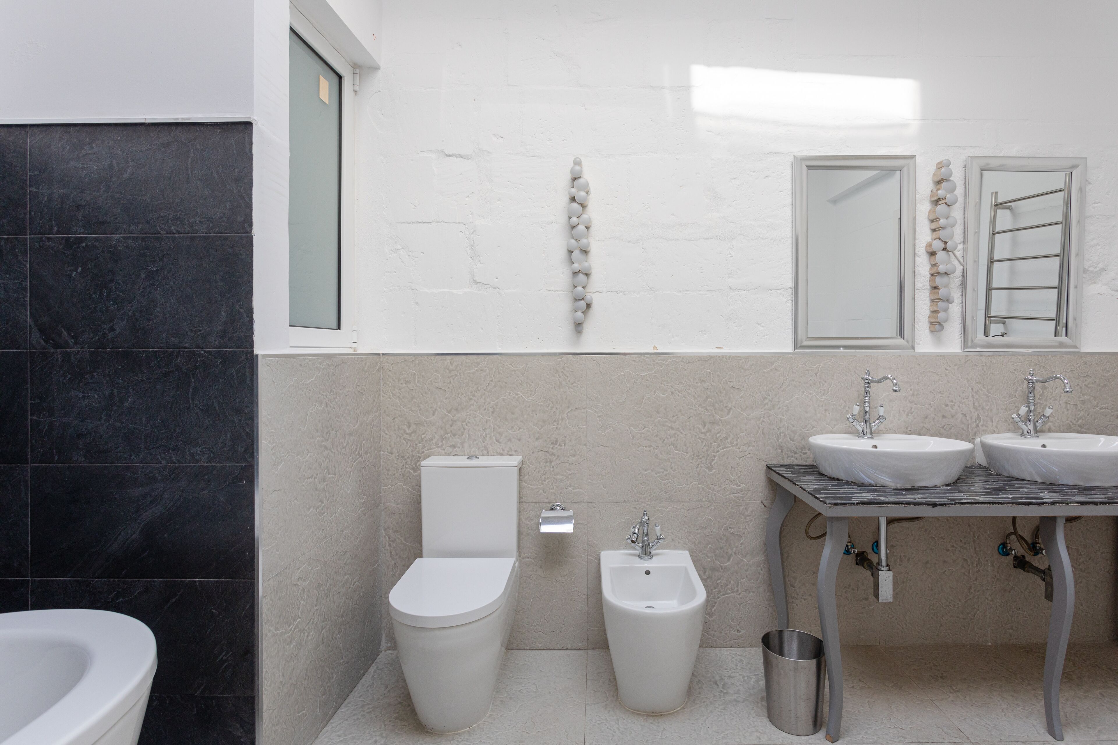 A modern bathroom with a toilet, bidet, and two sinks on a tiled floor.