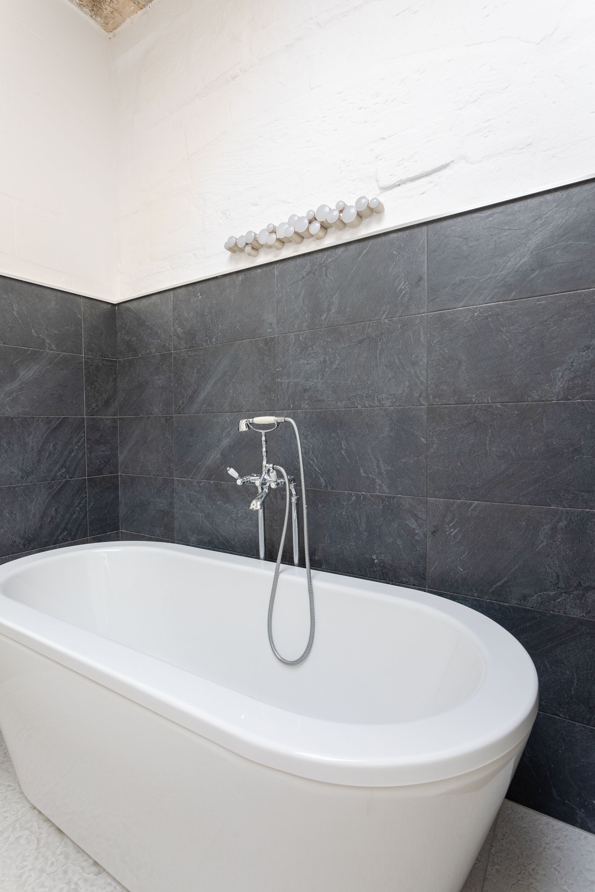 A modern bathroom with a freestanding bathtub, dark tiled walls, and a white ceiling.