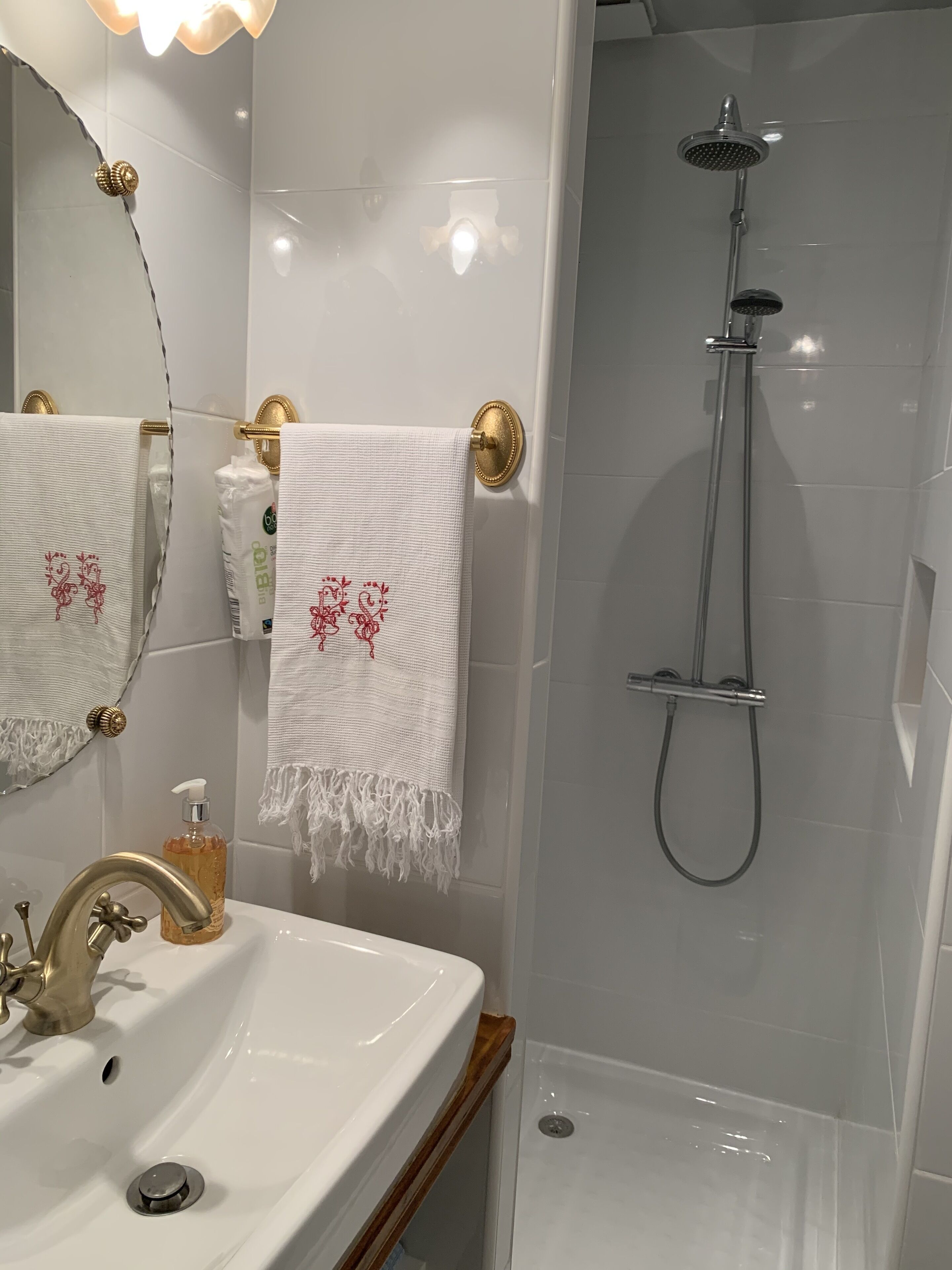 Une salle de bain avec un lavabo blanc, des robinets dorés, une douchette à main et des serviettes ornées de broderies rouges.
