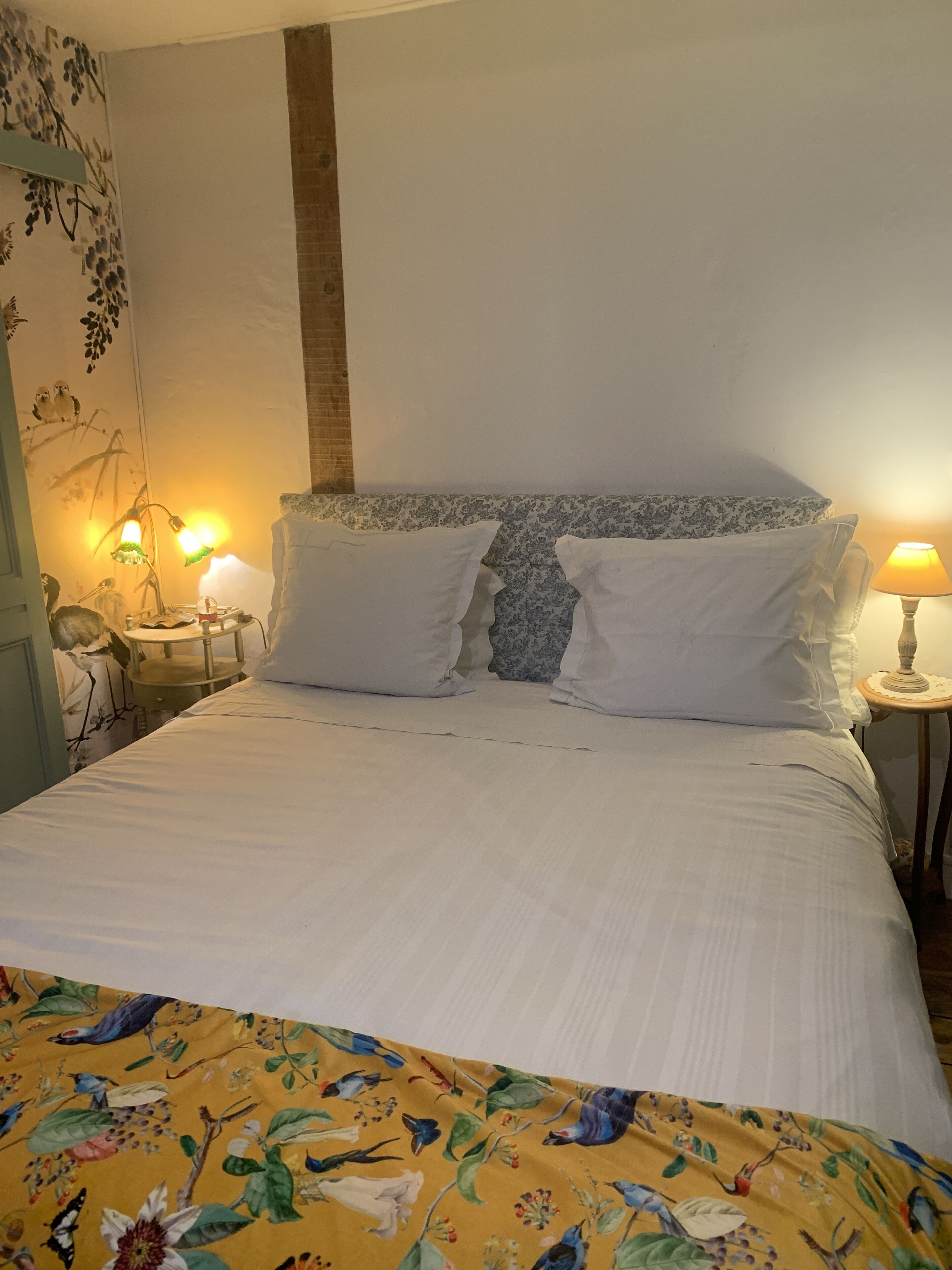 Una cama bien hecha con sábanas blancas y una colcha de cuadros florales, dos lámparas de noche y una pared con un mural floral.
