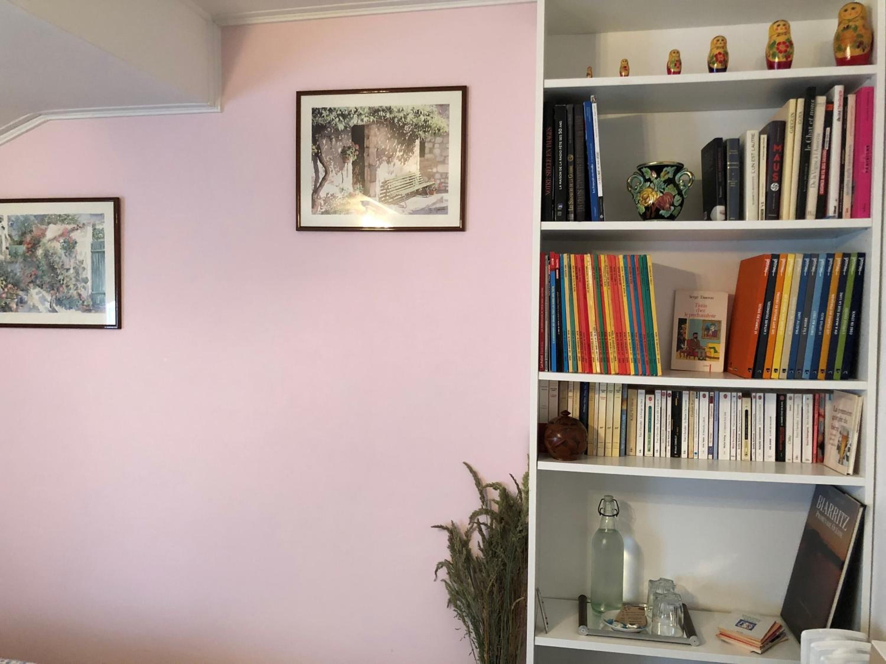 A room with a bookshelf filled with books, a framed picture on the wall, and a small decorative item on the shelf.