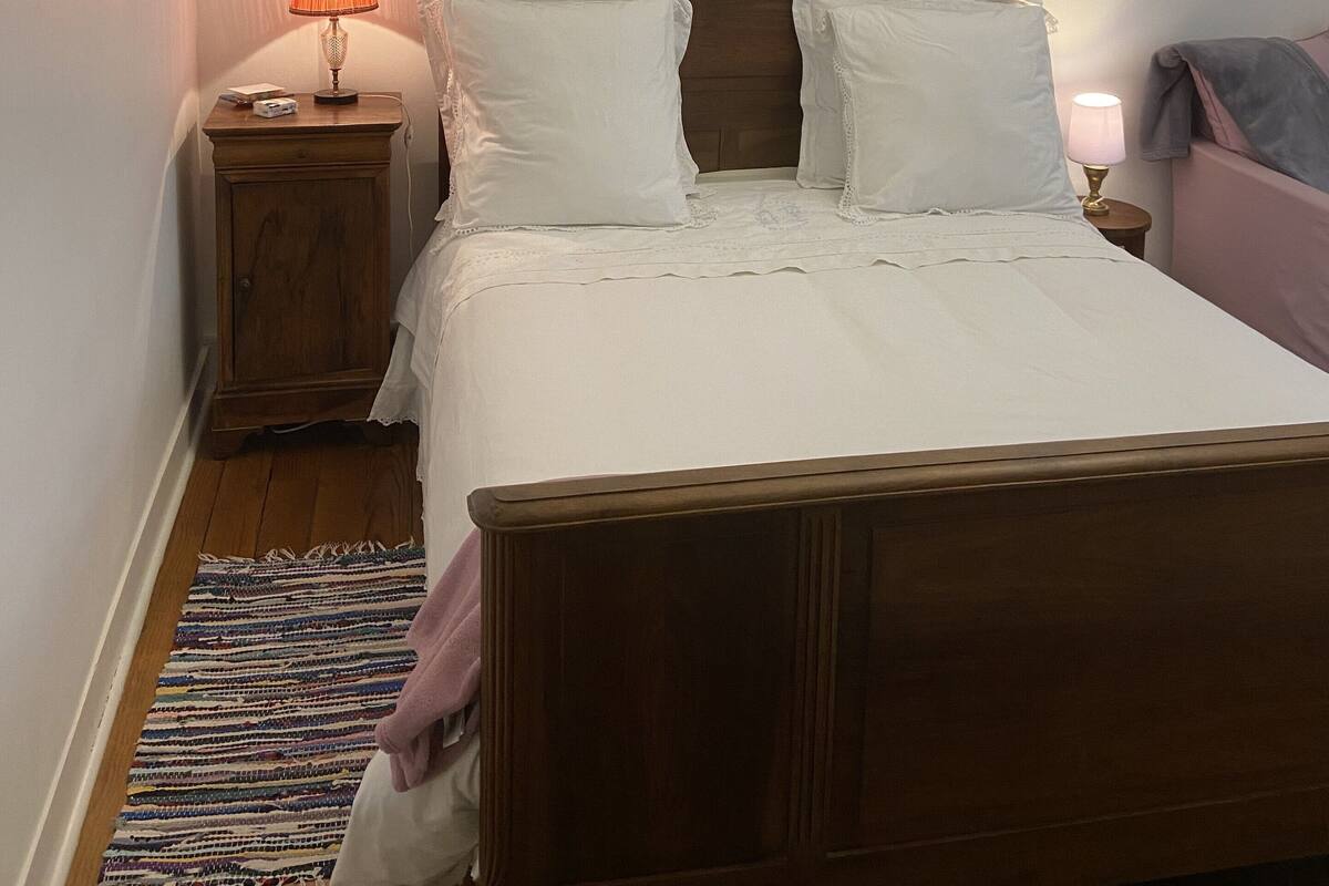 A neatly made bed with white linens, a wooden headboard, and two bedside lamps.