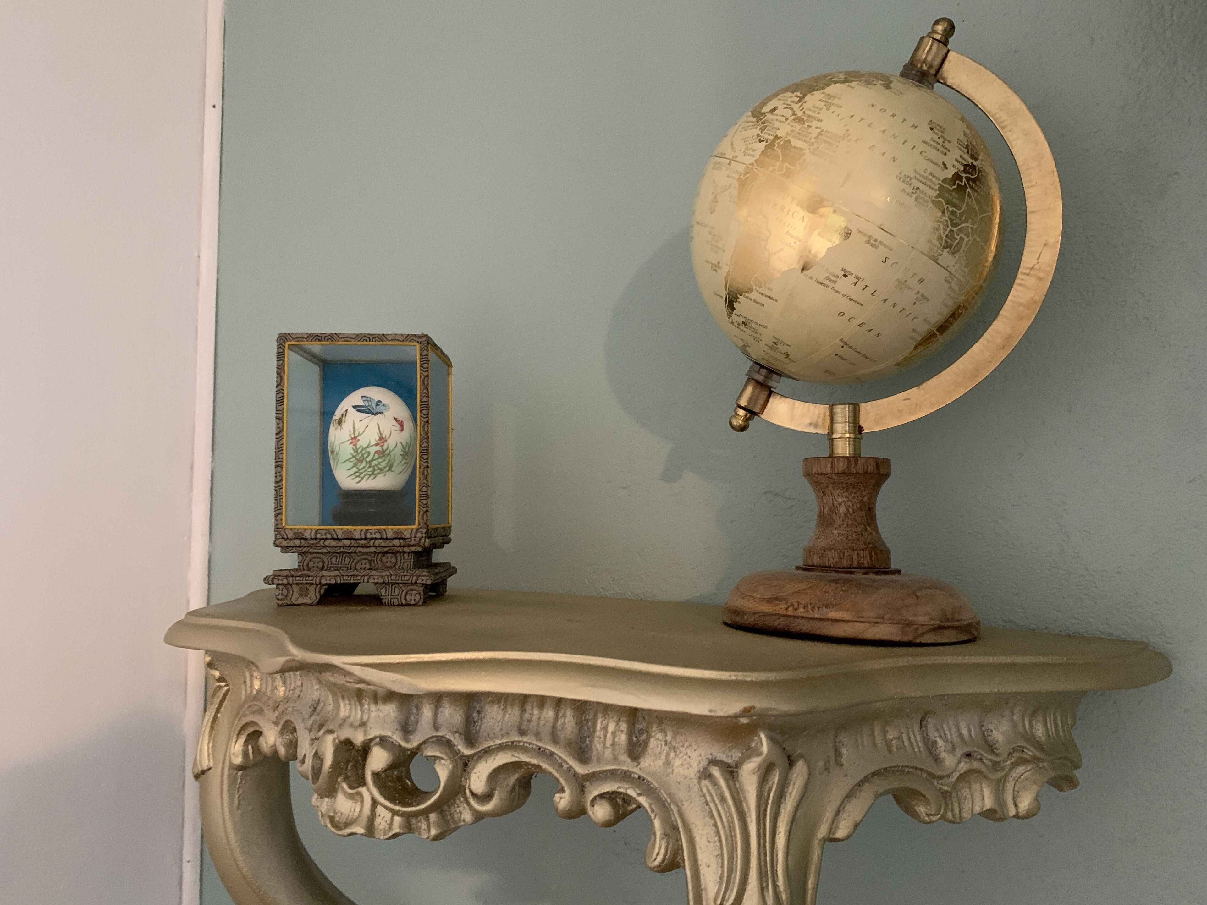 A globe on a wooden stand with a decorative base, placed on a table with ornate carvings.