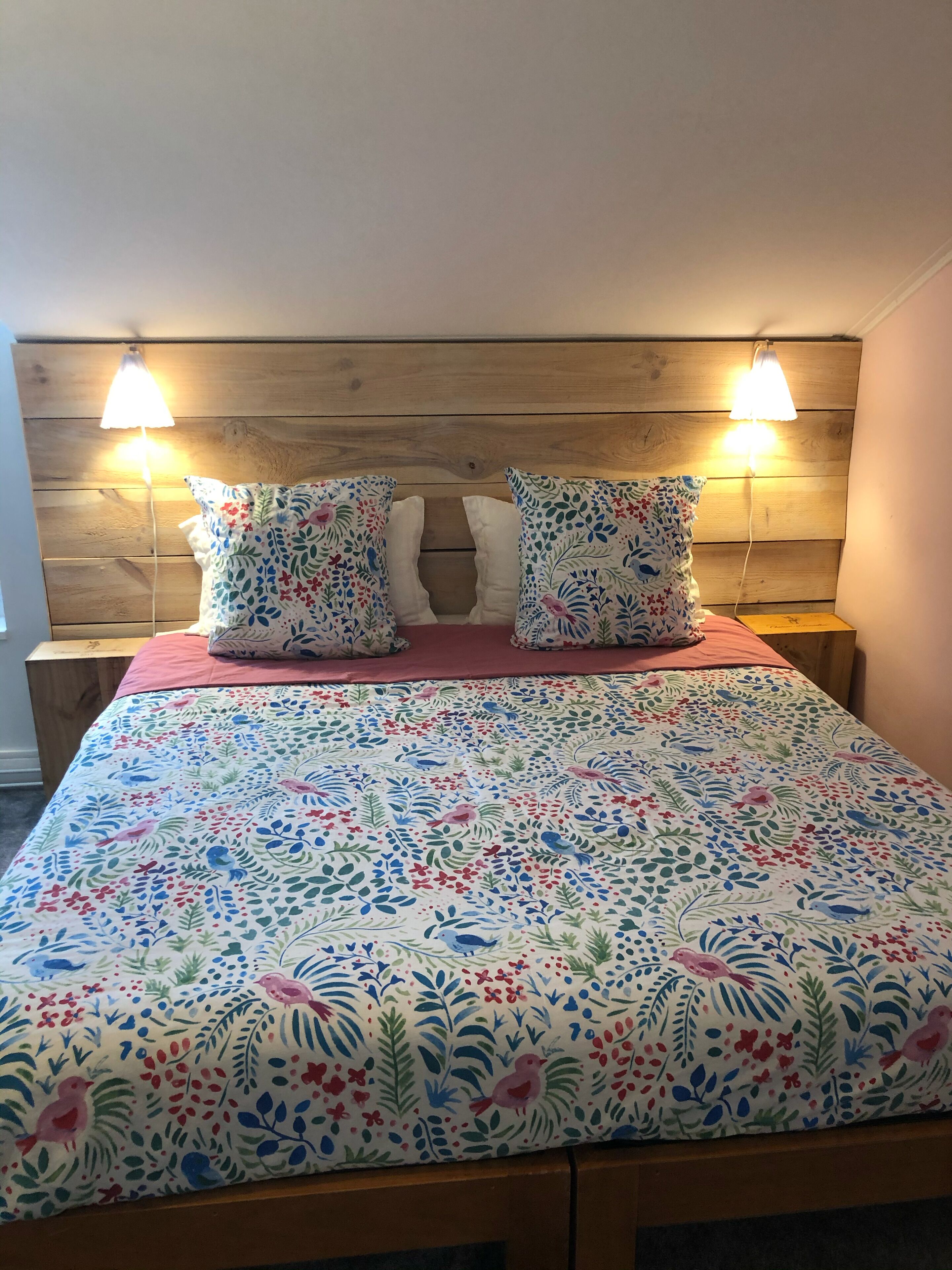 Una cama con colcha de estampado floral, dos almohadas blancas y dos lámparas de noche.