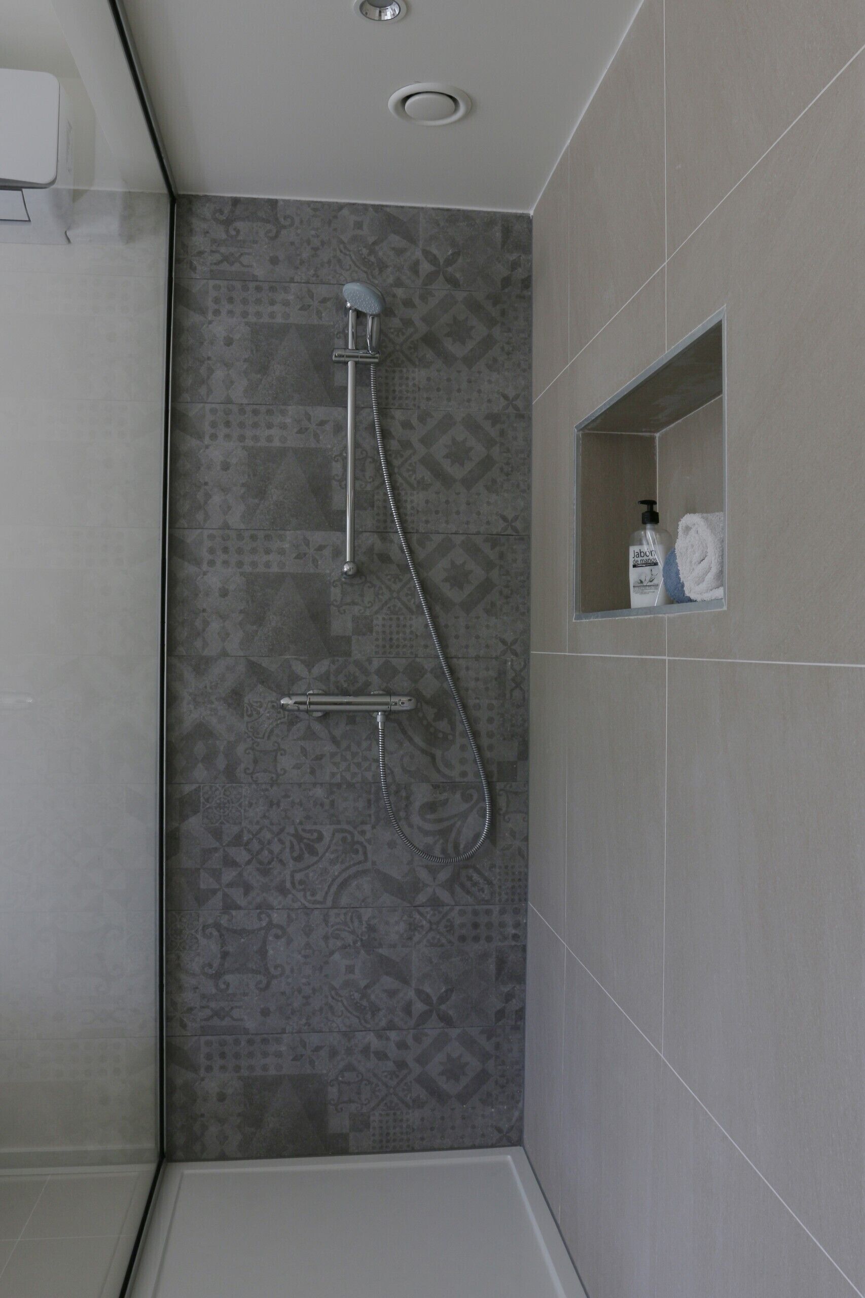 A shower area with a patterned tile wall, a built-in shelf with toiletries, and a handheld showerhead.