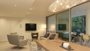 Un salon moderne avec une grande table à manger en verre, des chaises transparentes, un canapé et un téléviseur fixé au mur.