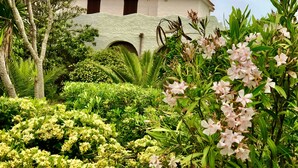 A building with a white facade and red-tiled roof, surrounded by lush greenery and flowering plants. - Sunsets in the sea of Sardinia (Sorso)