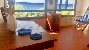 A room with a wooden table, a vase with dried flowers, a blue patterned tray, and a view of the sea through a window. - Sunsets in the sea of Sardinia (Sorso)