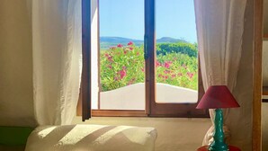A room with a large window, white curtains, a wooden frame, a teal lamp, and a white cushion on a green sofa. - Sunsets in the sea of Sardinia (Sorso)