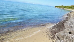 A beach with clear water, pebbles, and a distant shoreline. - Sunsets in the sea of Sardinia (Sorso)