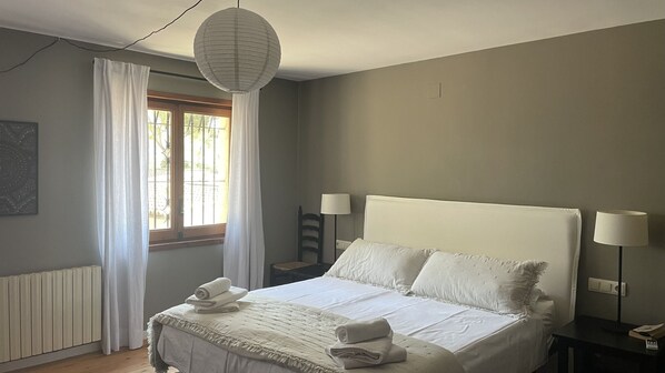 Et soveværelse med seng, to sengeborde med lamper, et vindue med gardiner, en radiator og en pendel.