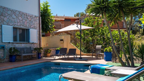 A swimming pool with lounge chairs, a patio area with a table and chairs, and a stone wall with a window. - Villa Vuelta , spacious house with private pool (Pals)