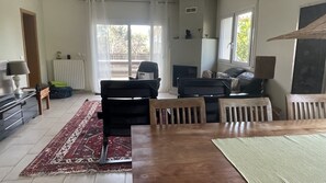 A living room with a sofa set, a dining table, and a view of the outdoors through a window.