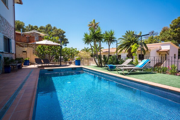 A swimming pool with lounge chairs, a patio area, and a building with a balcony.
