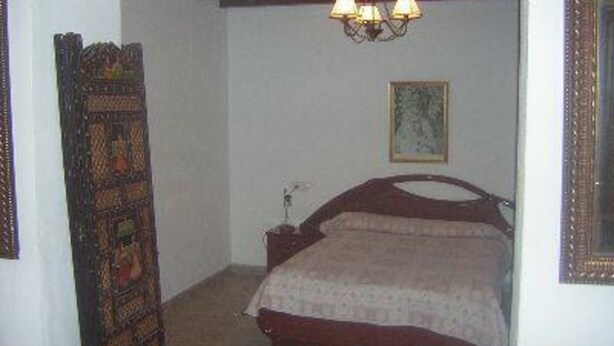 A bedroom with a wooden bed, a nightstand, a lamp, and a framed picture on the wall.