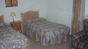 A room with two single beds, a nightstand with a lamp, and a plaid chair.