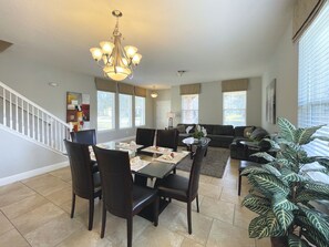 A dining area with a chandelier, dining table, chairs, and a sofa.