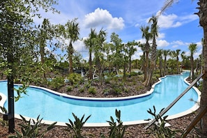 Une piscine entourée de palmiers et d’autres plantes vertes, sous un ciel bleu azur.