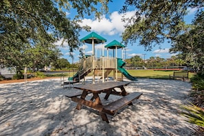 Enjoy a family-friendly park with a playground, picnic table, and bench surrounded by trees.