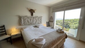 Un dormitorio con una cama grande, cabecera, mesita de noche, una silla, ventana con vistas y una calavera de toro montada en la pared.