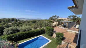 Une piscine avec vue sur un paysage vallonné et un espace patio aménagé avec du mobilier d’extérieur.